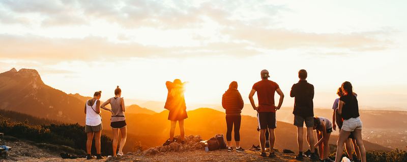 A group of people standing on a mountain ridge at sunset, seen from behind